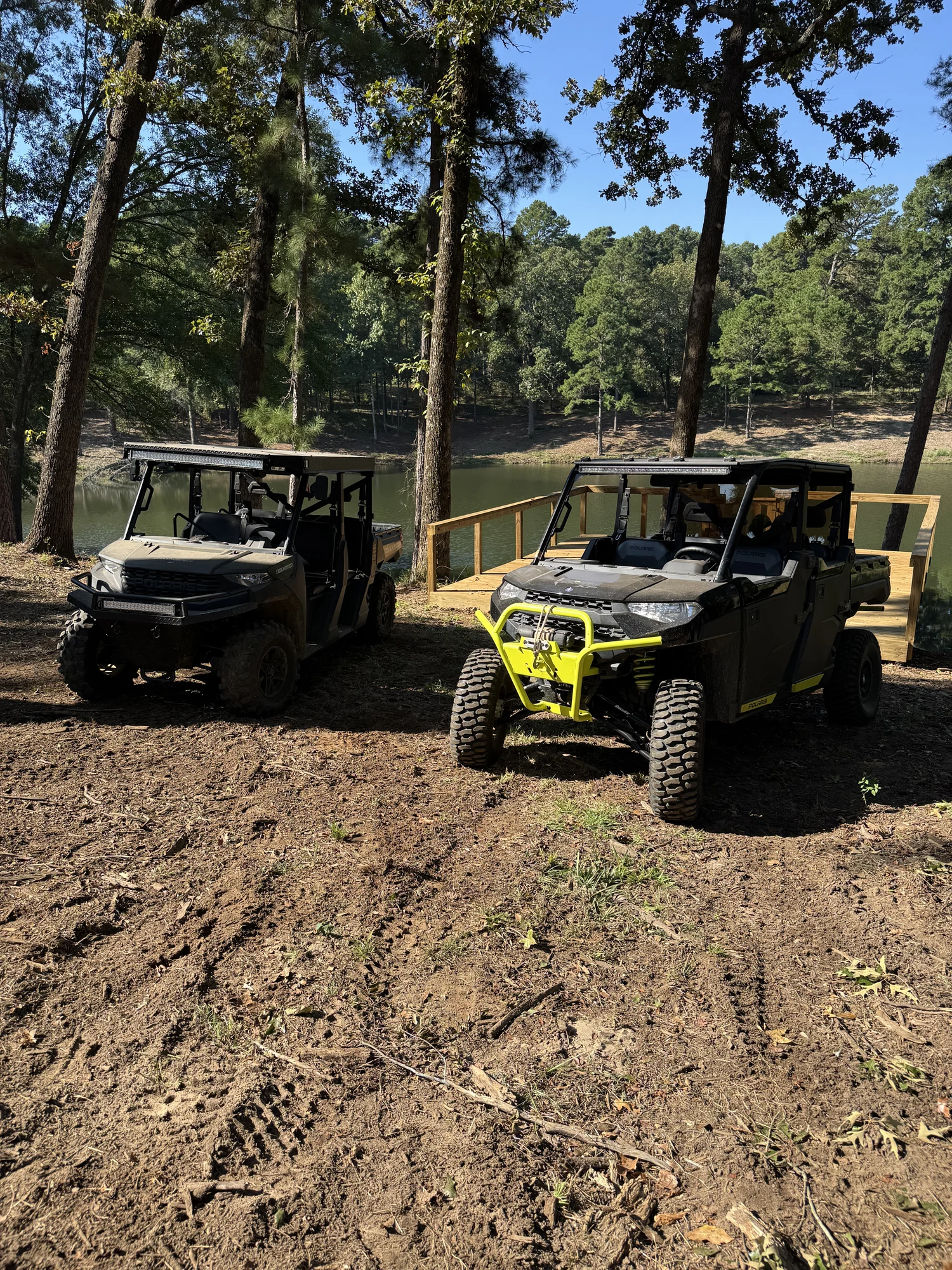 Two Polaris Ranger UTVs parked beneath trees beside the lake